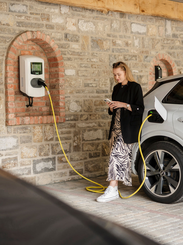 Frau schaut aufs Handy beim Laden eines E-Autos